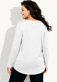 Biała koszula z długim rękawem i okrągłym dekoltem, z zaokrąglonym dołem. Miękka w dotyku i o swobodnym kroju. Noszona z ciemnymi dżinsami, prezentująca luźny styl.