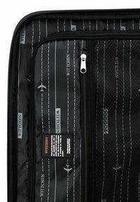 Interno di una valigia nera caratterizzato da una trama liscia con motivi bianchi a tema di viaggio, tasche in rete e molteplici scomparti con zipper per l'organizzazione.