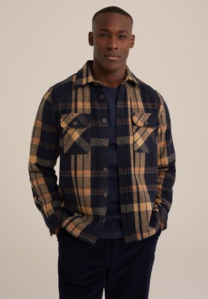 Navy and tan plaid flannel jacket with a buttoned front, two chest pockets, and a structured collar. Soft texture, long sleeves.