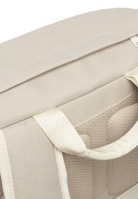 Bézs szövet táska texturált felülettel, párnázott pántokkal és erős varratokkal. Simább fedéllel és kontrasztos világos pántokkal rendelkezik.