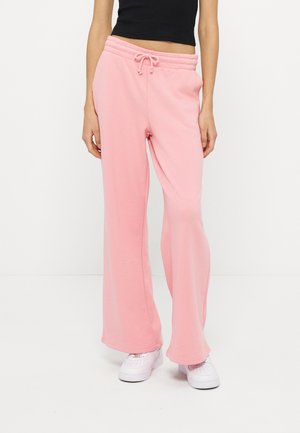 Kobieta w luźnych, jasnoróżowych spodniach dresowych z wiązanym pasem i białymi tenisówkami, w połączeniu z krótkim czarnym topem.