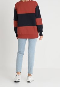 Czerwono-granatowy sweter w stylu color-block z klasycznym okrągłym dekoltem, miękką tkaniną i ribbowymi mankietami, w połączeniu z jasnoniebieskimi obcisłymi dżinsami i białymi trampkami.