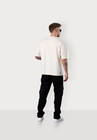 Short-sleeve cream cotton t-shirt with a relaxed fit, paired with black cargo pants and white sneakers. Includes a small logo detail on the shirt.
