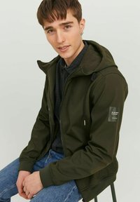 Olive green zip-up jacket with a hood, featuring a soft inner lining, adjustable drawstring, and a patch on the left sleeve.