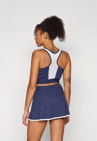 Marine sports-bh med et hvitt nettpanel, med racerback-design. Pairing med en matchende utsvingt skjørt med hvit kant.