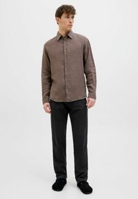 Brown linen shirt with a button-up design, featuring a pointed collar and long sleeves. Paired with black trousers and dark footwear.