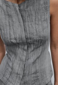 Graues, ärmelloses Oberteil aus Leinen mit einer zerknitterten Textur, das ein Überkreuz-Frontdesign und eine lockere Passform aufweist. Betont den sanften Fall und die natürlichen Fasern.