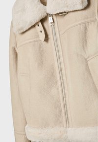 Béžová umelá shearling bunda so zipsom, veľkým kožúškom, hladkou textúrou a bočnými vreckami. Obsahuje švy so dekoratívnym stehom.