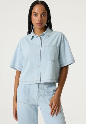 Hellblaues Jeanshemd mit kurzen Ärmeln, Kragen und Brusttasche. Verfügt über ein kurzes Design und dezente Nähte.