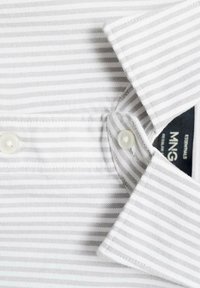 Camisa blanca con rayas gris claro, con un cuello abotonado, botones blancos y una etiqueta de tela visible en el interior del cuello.