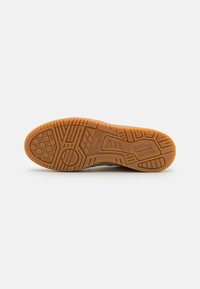 Suola in gomma di sneaker con un motivo texture, caratterizzata da scanalature e aree in rilievo per la trazione; colore arancione con una finitura liscia.