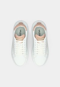 Biele tenisky s hladkým koženým zvrškom, ružovými akcentmi na päte a bielymi šnúrkami. Majú textúrovanú podrážku a značkové vnútro.