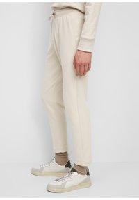 Licht beige sweatpants met een trekkoord in de taille, zijzakken, taps toelopende benen en een zachte textuur. Draagt met witte en olijfgroene sneakers.