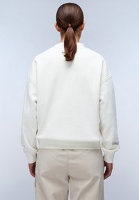 Crème sweatshirt met een ontspannen pasvorm, geribbelde mouwen en onderrand. Glad textuur. Gekocht met lichtbeige broeken. Minimalistische stijl.