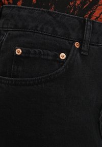 Svarta denimjeans med slim fit, koppardetaljer och detaljerad sömnad runt fickorna. Texturen verkar mjuk med en lätt stretch.