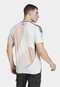 Camisola desportiva masculina em branco com desenhos geométricos abstratos em tons pastéis. Apresenta textura em malha, decote redondo e listas azul-marinho contrastantes nos ombros.