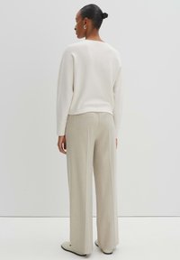 Felpa over-size di colore crema con scollatura rotonda e polsini a coste, abbinata a pantaloni a gamba larga in morbido tessuto di un beige chiaro e con vita alta.