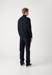 Dark navy pullover with a high collar, ribbed cuffs, and hem; paired with dark pants and black sneakers. Smooth texture, minimalist design.