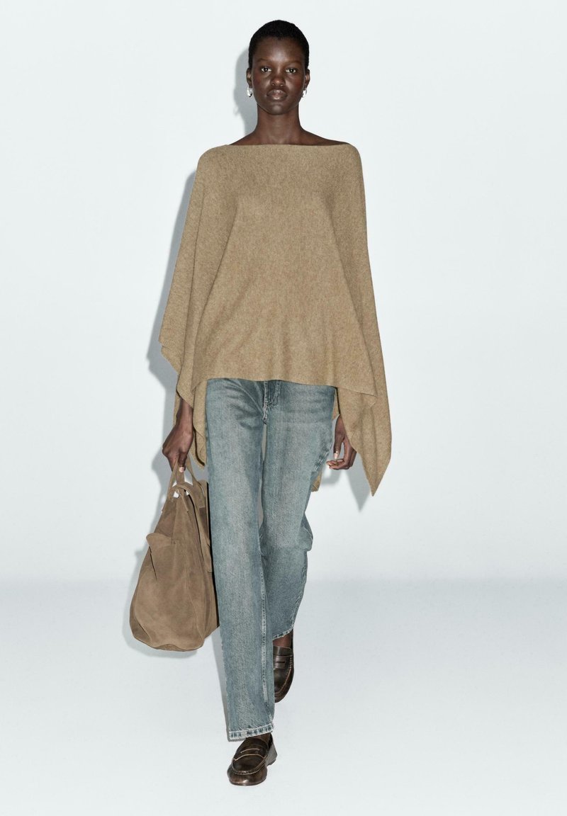 Un pull beige surdimensionné avec un col bateau, associé à un jean bleu clair et des mocassins marron. Porte un sac à bandoulière en peau de daim beige.