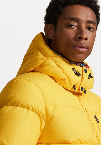 Yellow puffer jacket with a high collar, featuring black hardware accents and a patterned interior lining. Soft, quilted texture visible.