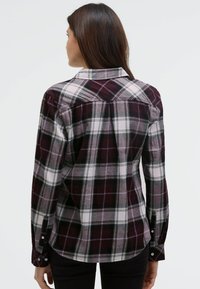 Long-sleeve plaid shirt in dark burgundy, black, and white. Features a buttoned collar and cuff, with a curved hem and shoulder yoke detail.