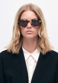 Aurinkolasit, joissa on kilpikonnakuosiset pyöreät linssit, mustalla kehykset linssien ympärillä ja kiiltävä pinta. Kevyt muotoilu.