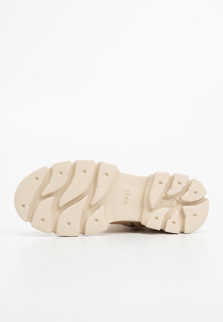 Suela de zapato beige con surcos profundos y segmentados y hendiduras circulares, posicionada horizontalmente sobre un fondo blanco.