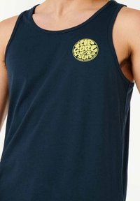 Marineblå tanktop lavet af blødt bomuld, med et rundt gult logo på venstre brystområde, og et klassisk ærmeløst design.