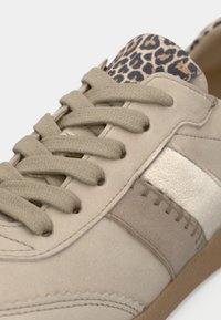Μπεζ αθλητικό παπούτσι με υφή σαουέτ, μεταλλική ασημί ρίγα και λεπτομέρεια με σχέδιο λεοπάρ στο τακούνι. Σχεδίαση με κορδόνια από ύφασμα.