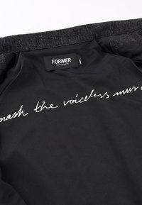 Εσωτερικό μαύρου μπουφάν που δείχνει την ετικέτα της μάρκας "FORMER" και λευκό καλλιγραφικό κείμενο που διαβάζεται εν μέρει ως "smash the voiceless music".