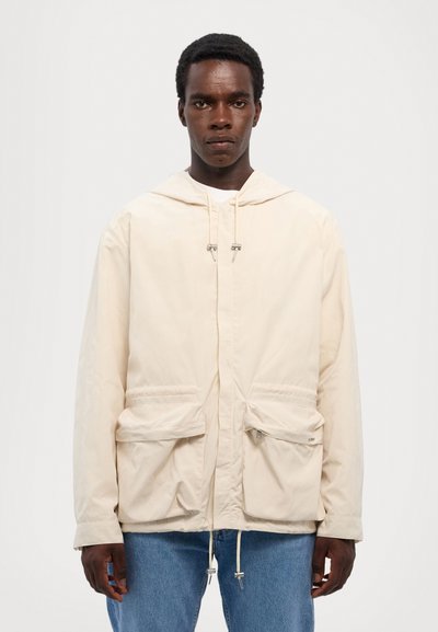 Svetlo bež jopica s kapuco, izdelana iz lahke tkanine, z dvema sprednjima žepoma, nastavljivimi vrvicami in sproščenim krojem.