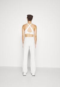 Bílá sportovní podprsenka s křížovými ramínky a otevřeným zadním dílem, v kombinaci s volnými, světlými šedými tepláky a stříbrnými teniskami.