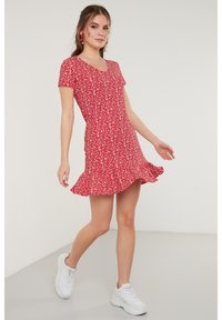 Rode bloemen jurk tot op de knie met korte mouwen, v-hals en uitlopende zoom. Gepaard met witte sneakers voor een casual uitstraling.