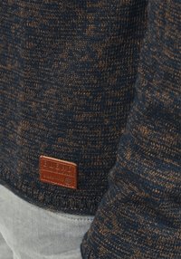 Maglione lavorato a maglia di un blu scuro con un motivo testurizzato, con dettagli marroni. Include un'etichetta in pelle marrone con la scritta "BLEND" in basso.