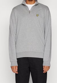 Felpa grigia con collo a mezza zip, polsini e orlo a coste. Presenta un piccolo logo giallo sul petto a sinistra. Tessuto dalla texture morbida.