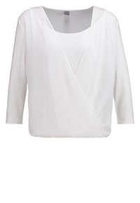 Blouse blanche à enrobage avec un décolleté en V profond, des manches trois-quarts et un tissu doux et léger. Présente une texture lisse et un design minimaliste.