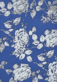 Kwiatowy materiał ma niebieskie tło z białymi wzorami róż i zielonymi liśćmi. Wzór jest tkany z teksturowanym wykończeniem.