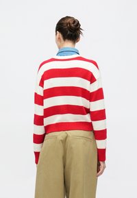 Κόκκινο και λευκό ριγέ πουλόβερ με άνετη εφαρμογή, ριμπ τελείωμα και μανίκια με μανσέτες, σε συνδυασμό με χακί παντελόνι. Ανοιχτό μπλε γιακάς εμφανίζεται από κάτω.