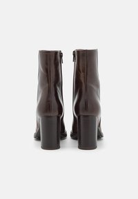 Bottes basses en cuir marron, avec une texture lisse, un bout arrondi et un talon haut épais. Fermeture éclair arrière avec des détails de couture minimalistes.