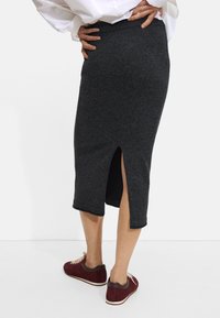 Ciemnoszara, spódnica długości do kolan wykonana z miękkiego dzianinowego materiału, z bocznym rozcięciem. Noszona z burgundowymi butami i schowaną pod białą koszulą.