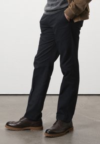 Pantalons navy avec une coupe droite, dotés de poches latérales. Portés avec des richelieus marron foncé en cuir texturé et une semelle contrastante.