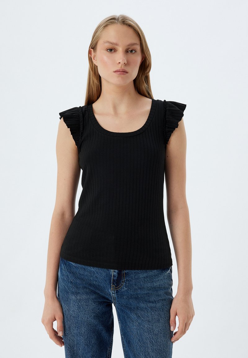 Mustikka ribbikangas tank top, jossa on avara kaula-aukko ja röyhelökoristeet olkapäillä. Yhdistetty vaaleansinisiin farkkuihin.