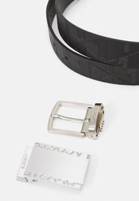 Cinturón negro texturizado con dos hebillas metálicas intercambiables; una rectangular plateada con logo grabado, y otra plateada con un diseño clásico de marco.