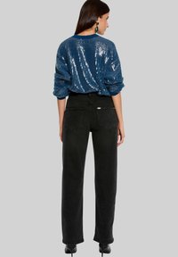Jeans noirs taille haute à coupe droite, associés à un pull bleu texturé orné de sequins. Le pull présente un design côtelé et des manches longues.