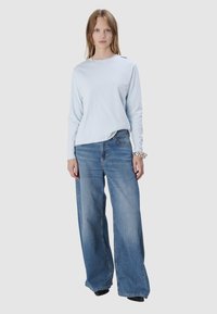 Hellblaues Langarmshirt mit rundem Ausschnitt; kombiniert mit locker sitzenden, hellblauen Denim-Jeans mit weitem Bein. Silbernes Armband als Akzent.