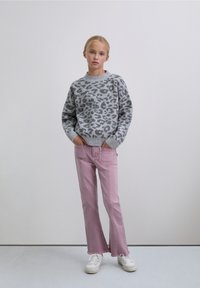 Suéter gris con estampado de leopardo y cuello redondeado, combinado con jeans acampanados de color rosa claro. La modelo lleva zapatillas blancas, de pie con las manos en los bolsillos.