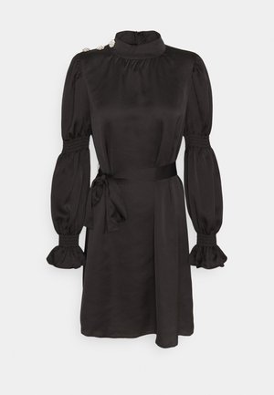 Vestito in raso nero con collo alto, maniche lunghe a sbuffo con polsini arricciati, bottoni sulle spalle e cintura da annodare in vita.