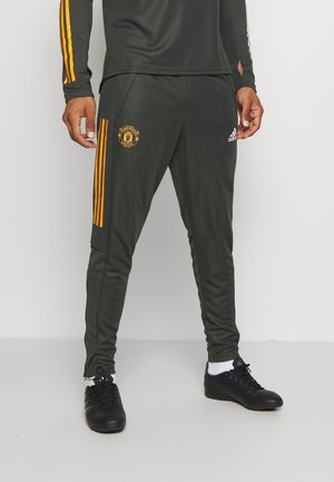 Man draagt zwarte sportbroek met oranje Manchester United-logo, oranje zijstrepen, wit Adidas-logo, zwarte schoenen en witte sokken.