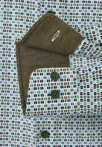 Koszula z kołnierzykiem wykonana z białej tkaniny z geometrycznym wzorem w zielonym, niebieskim i czarnym kolorze. Posiada zielone guziki oraz kontrastowy brązowy wnętrze kołnierza.