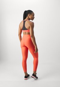 Lys korallfarget treningsgenser og matchende tights laget av stretchstoff. Tightsene har en logo på siden og en glatt overflate. Sorte joggesko.